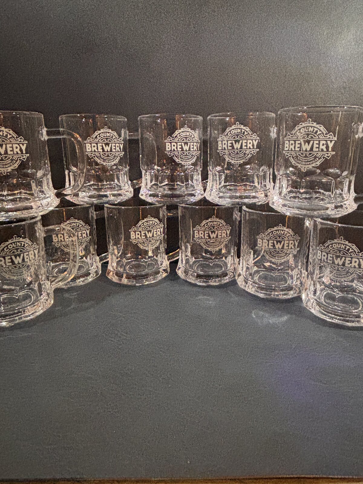 Collection of miniature glass beer mugs engraved with the County Brewing Company logo